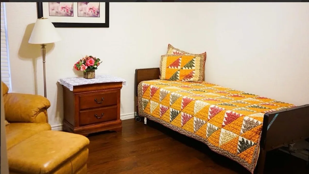 A resident bedroom at Heritage Touch, made up with an autumn quilt beside a lamp and nightstand